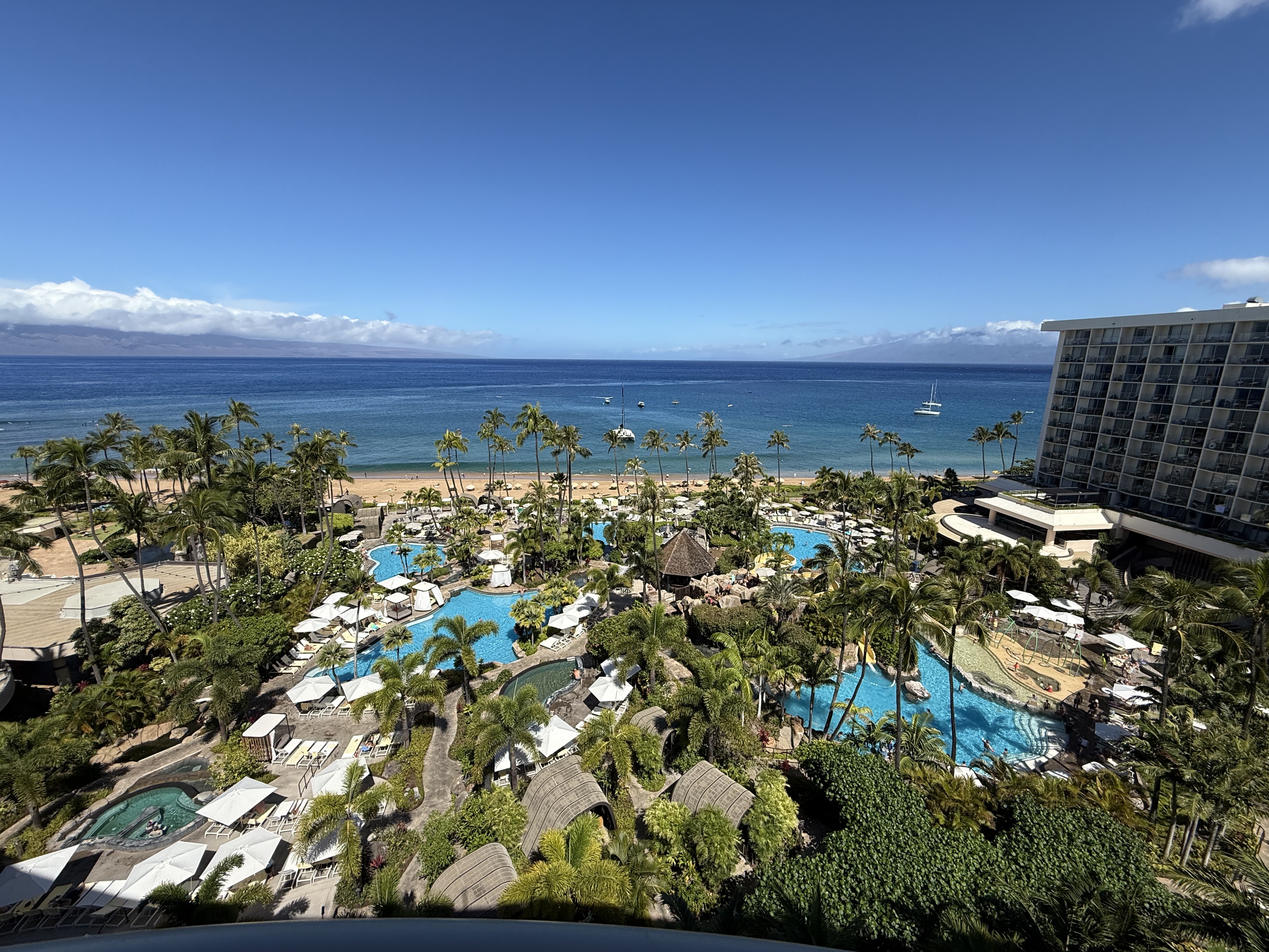 Aerial view of a Ka'anapali resort at sunset with palm trees and a curved pool overlooking the Pacific